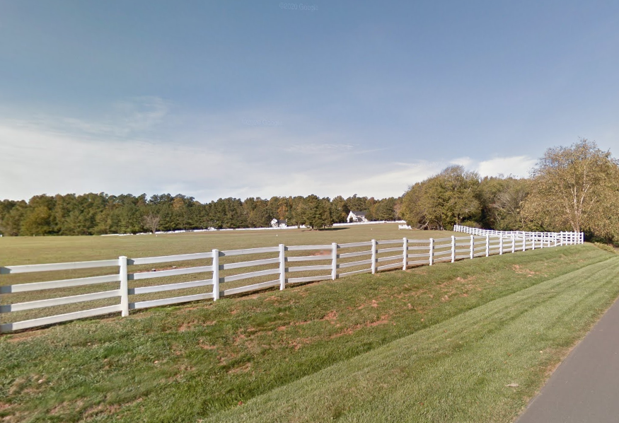 Entry drive into Hardscrabble Plantation neighborhood. White board fencing and green fields. 